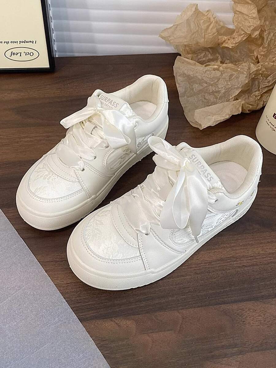 Top-front view of white platform sneakers with satin ribbon laces and floral embroidery