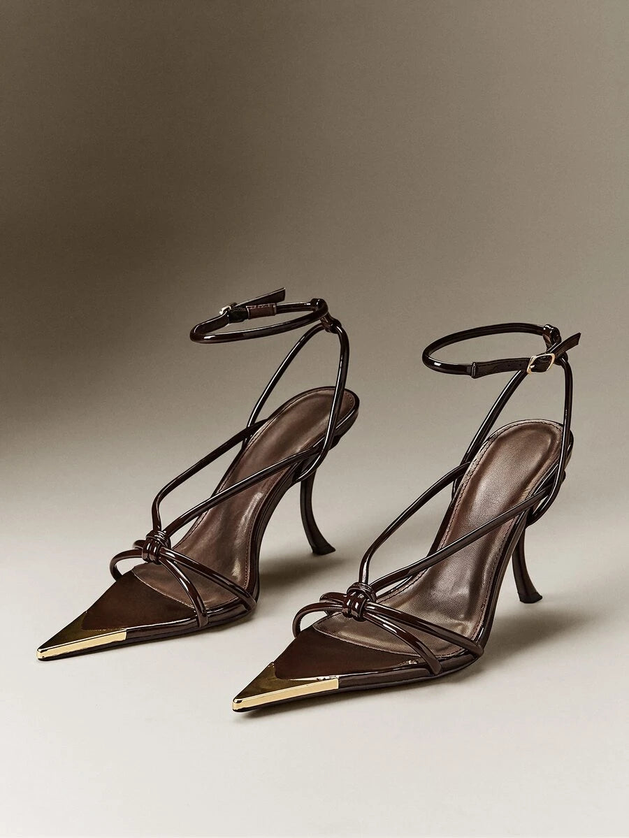Front three-quarter view of glossy chocolate-brown pointed-toe strappy stiletto sandals with ankle buckles