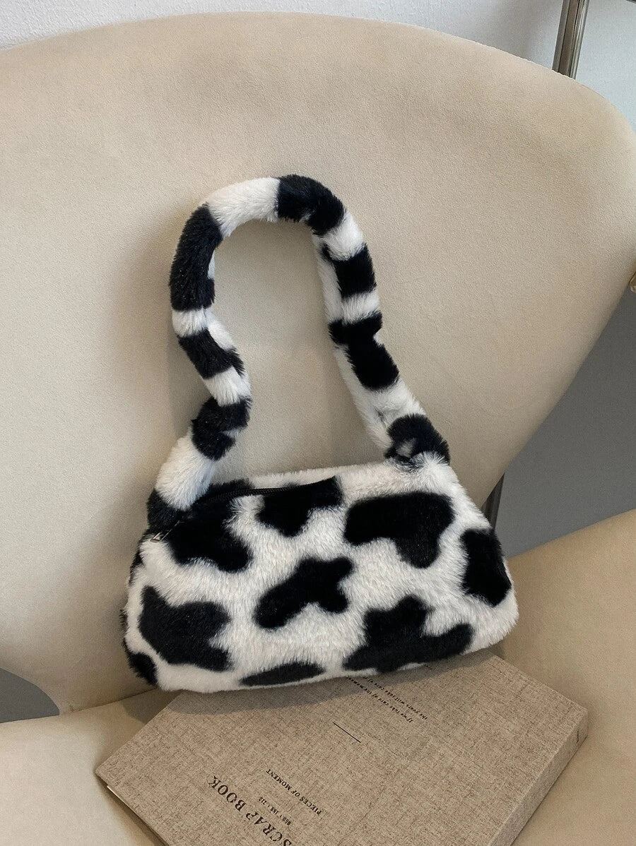 Cow-print plush baguette handbag with padded handle resting on cream chair