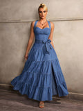 Full-length front view of a blue denim maxi dress with a bow waist belt, tiered ruffle skirt and high slit, styled with heels