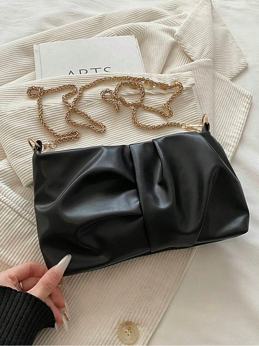Black ruched faux leather shoulder bag with gold chain strap on cream jacket