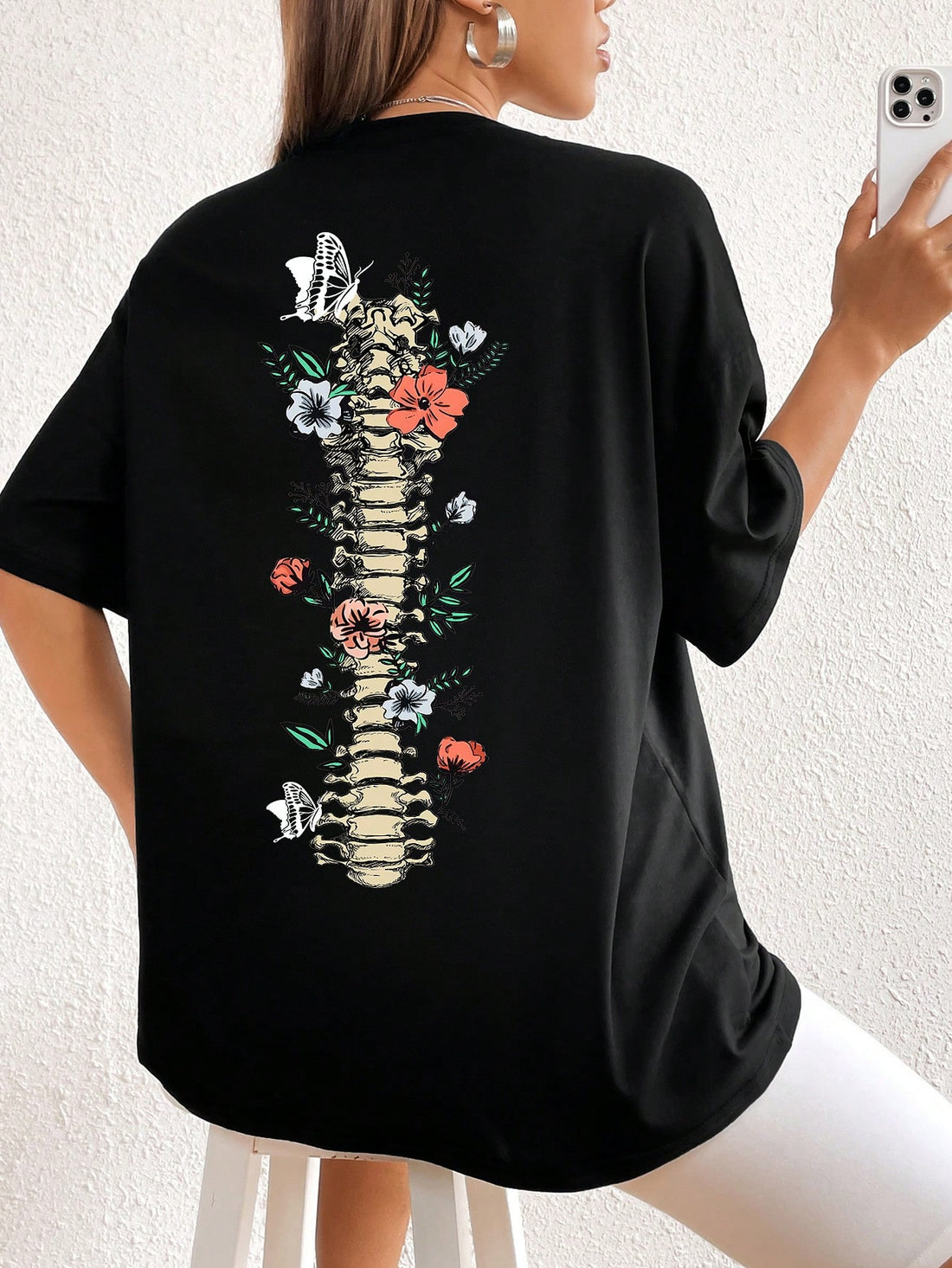 Introducing the Chic and Spooky: Floral Skeleton Print Drop Shoulder Tee. This t-shirt boasts a unique floral skeleton print, perfect for adding a touch of edge to any outfit. Its drop shoulder design offers a fashionable and comfortable fit. Get ready to stand out with this chic and spooky tee.