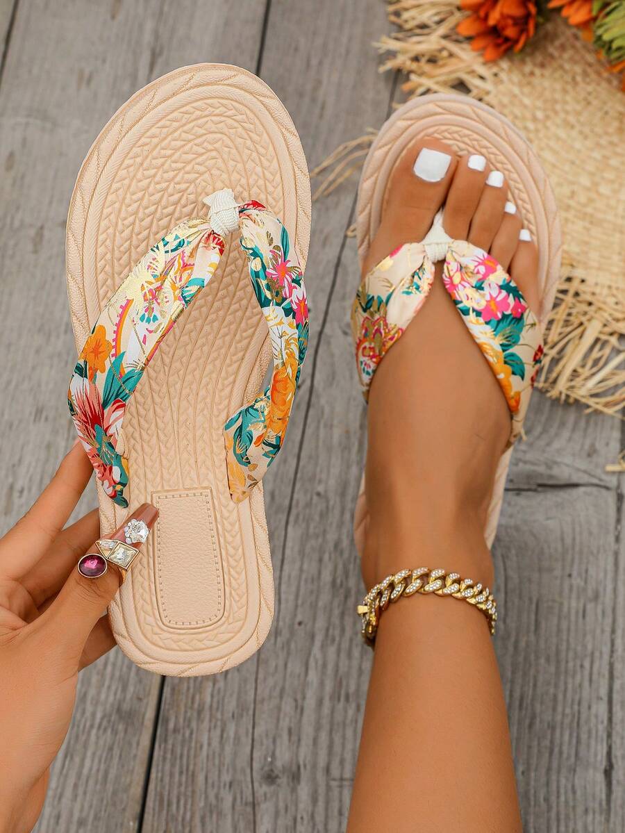 Overhead tropical floral beige flip-flops shown worn and held on a wooden deck