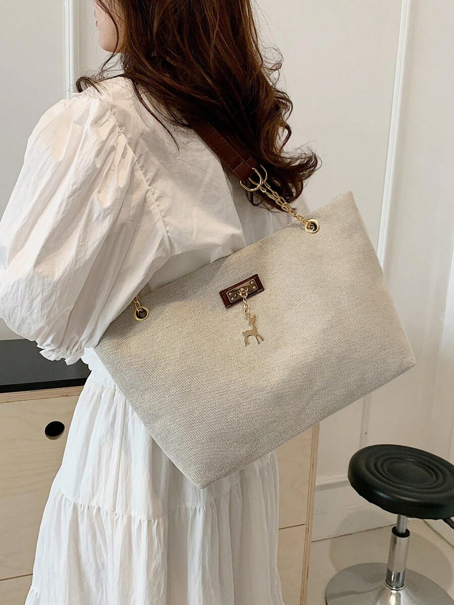 Model carrying beige woven texture tote bag over shoulder with brown strap gold hardware and deer charm