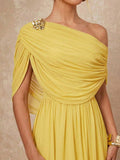 Yellow one-shoulder draped maxi dress with gold flower brooch