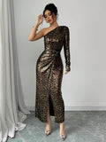 A woman models a long-sleeve, one-shoulder maxi dress with a metallic leopard print pattern in brown and gold. The dress features a draped waist and a high front slit.