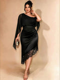 Front full-length view of black fitted midi dress with asymmetric neckline, flowing cape sleeves and lace hem