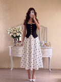 Front mirror view of black square-neck gold-button top and white polka-dot A-line midi skirt set
