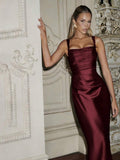 Front three-quarter view of burgundy ruched square-neck satin dress against ornate interior
