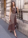 Front view of brown sleeveless midi dress with cream polka dots, diagonal stripes and asymmetric hem on a city street