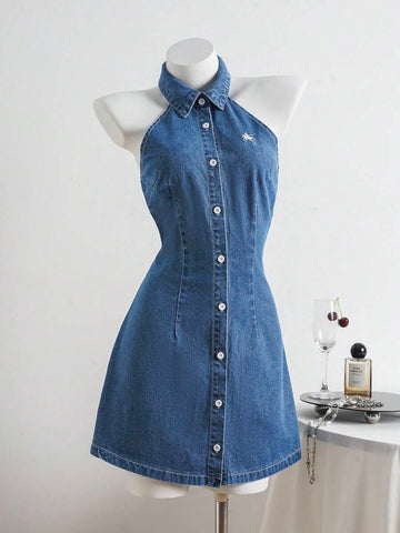 Full front view of medium-wash collared halter mini denim dress with buttons and white chest embroidery