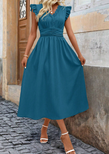A woman wearing a teal blue midi dress with ruffled cap sleeves, a scalloped V-neckline, and a gathered waist, standing outdoors against a rustic stone wall.