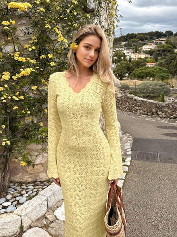 Front three-quarter view of yellow openwork knit maxi dress on a village road