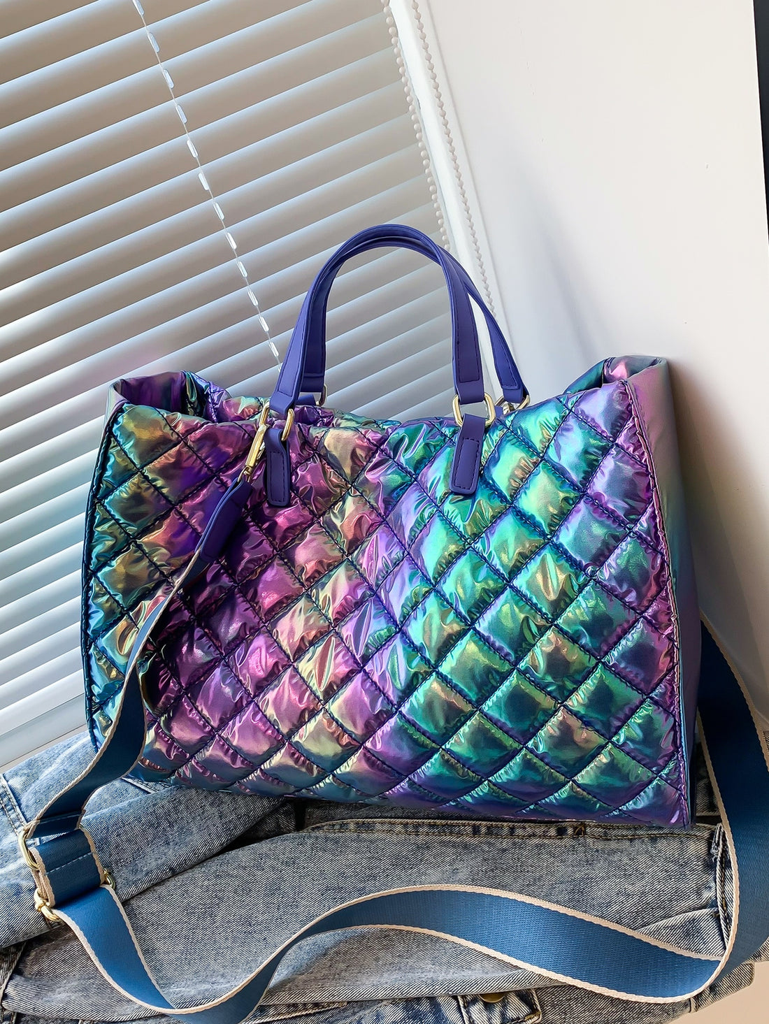 Catch the light and turn heads with this eye-catching holographic quilted top handle bag. The shimmering, iridescent finish shifts with every angle, making it the ultimate statement piece for anyone who loves bold style. Quilted detailing adds texture and dimension, while the sturdy top handle keeps your essentials secure and stylish. Whether you're heading to brunch, a night out, or just running errands, this bag brings that fun, futuristic vibe to any outfit. Compact yet spacious enough for your daily mus