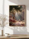 A framed art print depicting a serene outdoor landscape with sunbeams filtering through trees, hanging on a white wall above a wooden table with a cup and vase of dried flowers.