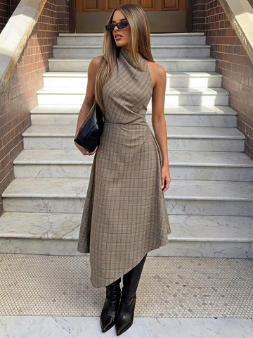 Three-quarter view of a khaki plaid sleeveless dress with high neckline and uneven draped hem on stone steps.