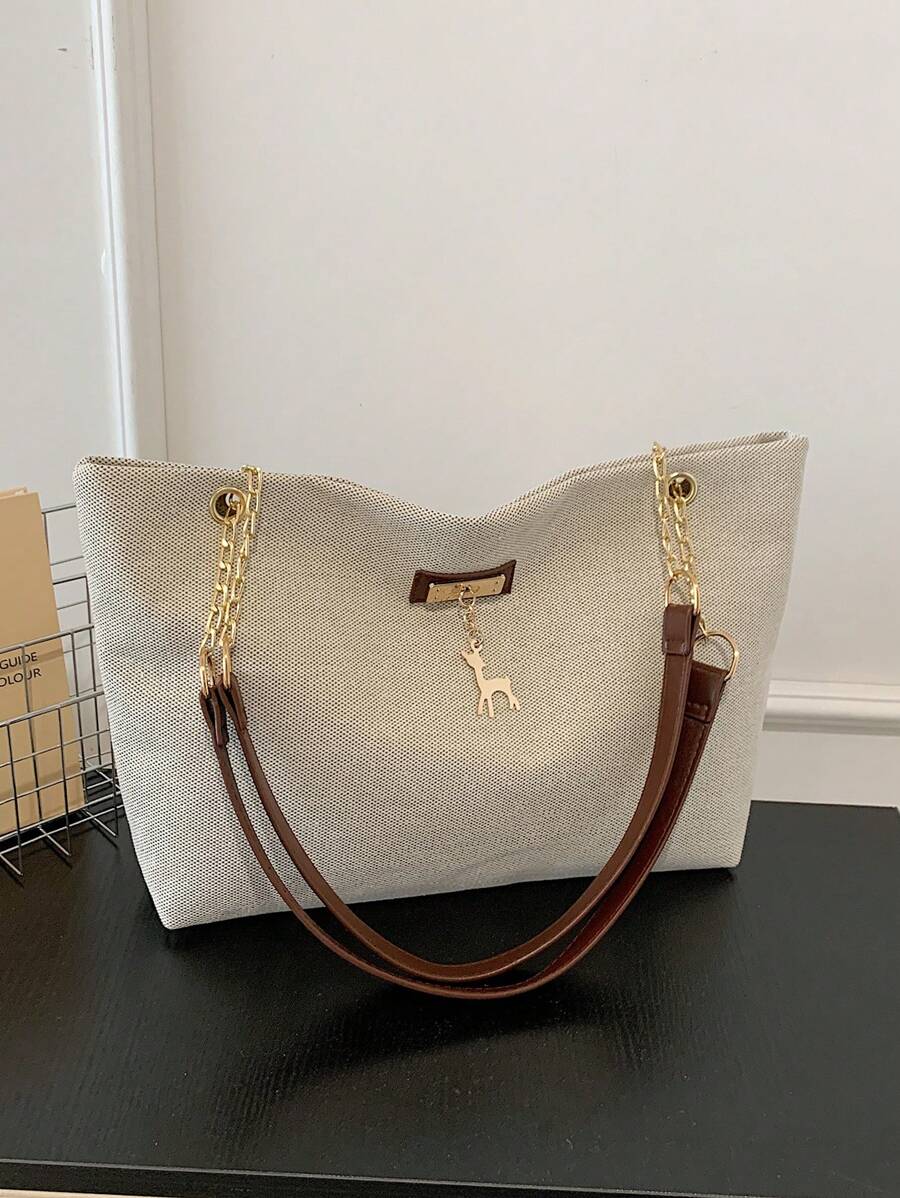 Beige large shoulder tote bag with brown straps gold chain hardware front plaque and hanging deer charm on black table
