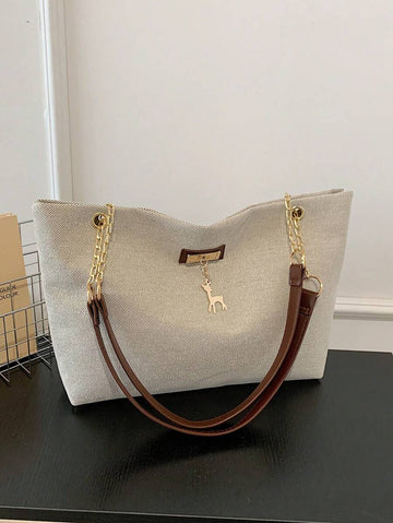 Beige large shoulder tote bag with brown straps gold chain hardware front plaque and hanging deer charm on black table