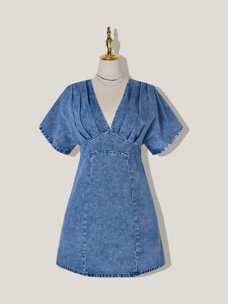 Front view of medium-wash denim mini dress with deep V neck and pleated high-waist bodice
