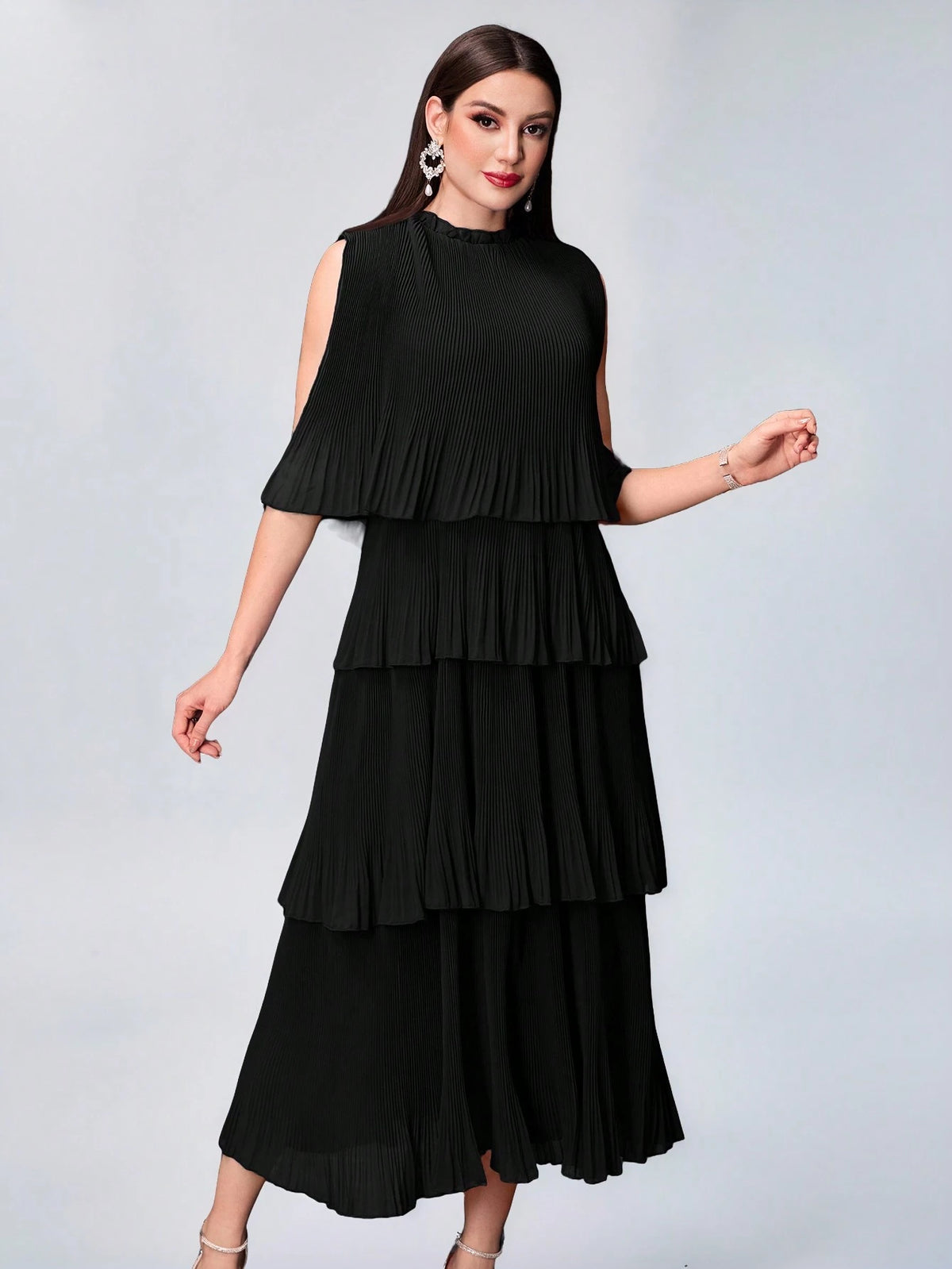 A woman modeling a sleeveless black midi dress with a tiered ruffled skirt and shoulder cutouts, photographed against a light gray studio background.