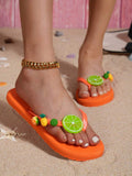 Front close-up of burnt orange fruit charm flip-flops worn on beach sand