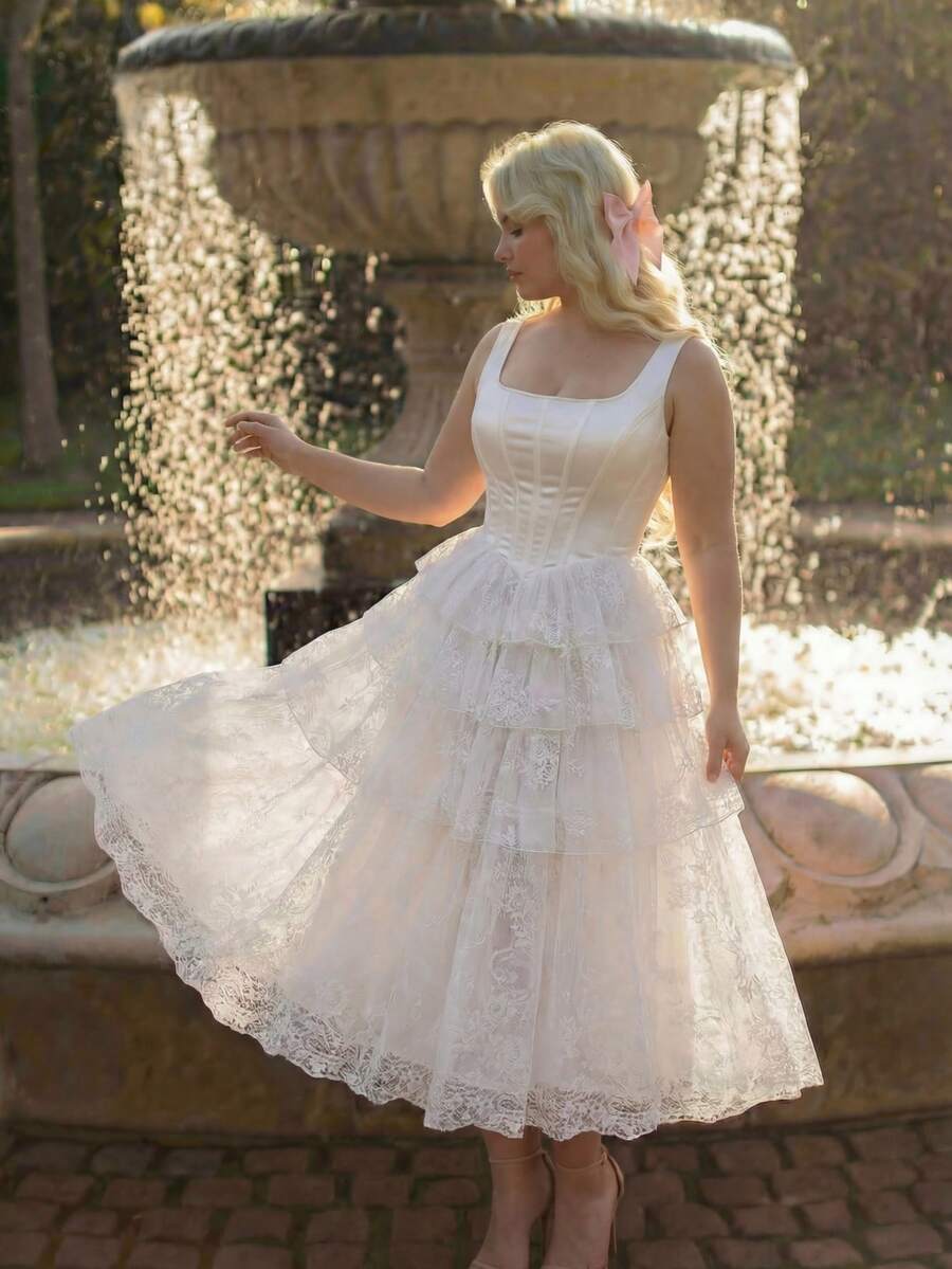 Full front view of white lace tiered midi dress beside a garden fountain