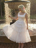 Full front view of white lace tiered midi dress beside a garden fountain