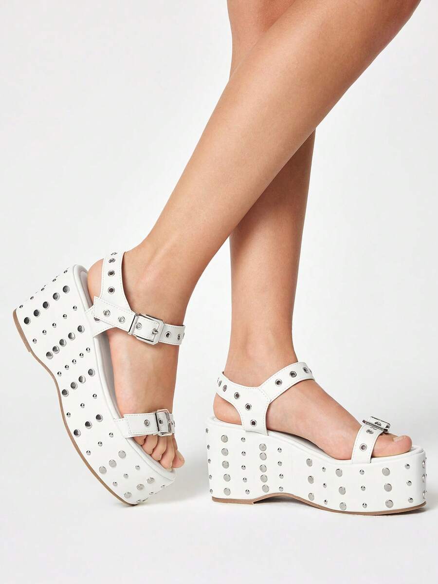 Make a bold statement this summer with these punk-inspired spike buckle heeled platform sandals. Featuring geometric spike detailing and a sturdy buckle closure, these open-toe wedge slides deliver edgy style with comfort. Crafted from premium PU leather with a durable TPR outsole, they're perfect for outdoor festivals and warm-weather occasions. The high platform heel adds confidence to any look while keeping you grounded. Available in crisp white to complement any summer wardrobe.