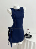 Front three-quarter view of dark indigo sleeveless denim mini dress with round neck and side tie bow