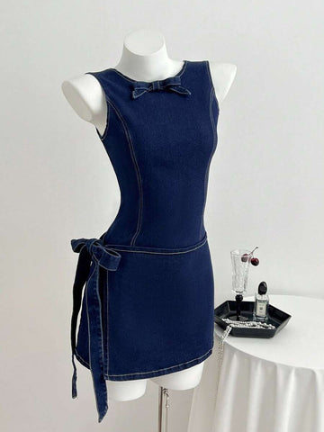Front three-quarter view of dark indigo sleeveless denim mini dress with round neck and side tie bow