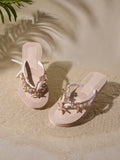 Top three-quarter view of blush beige platform flip flops with gold chains, pearls and sea charms on sand