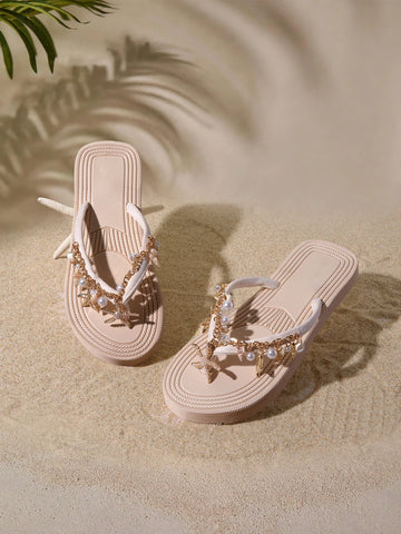 Top three-quarter view of blush beige platform flip flops with gold chains, pearls and sea charms on sand
