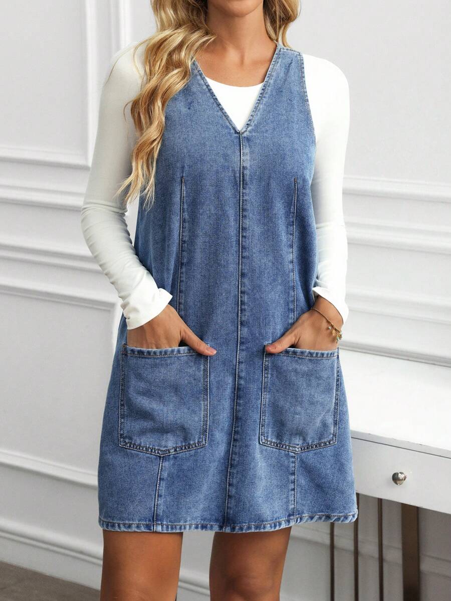 Front detail view of medium blue denim pinafore mini dress layered over a white long-sleeve top