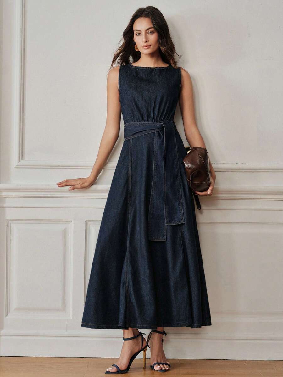 Full front view of dark indigo belted denim maxi dress styled with clutch and heels