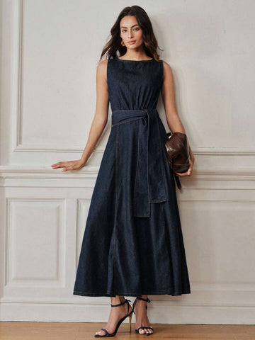 Full front view of dark indigo belted denim maxi dress styled with clutch and heels