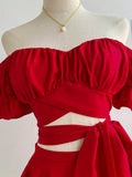 Close-up of red ruched off-shoulder crop top with puff sleeves, wrap front cutout, and pearl necklace