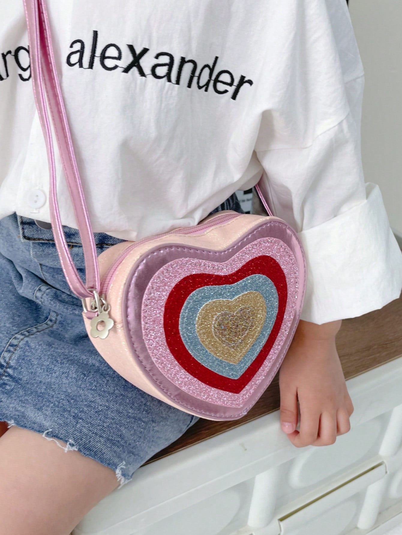 Introduce your child to style with our Sparkly Heart Shaped Mini Crossbody Bag. Crafted from synthetic leather, this trendy bag features a colorful color block design that is sure to make a statement. Perfectly sized for kids, your little one can carry their essentials with ease while adding a touch of sparkle to their outfit.