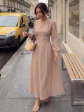 Front three-quarter street view of brown striped long-sleeve maxi dress with gathered waist