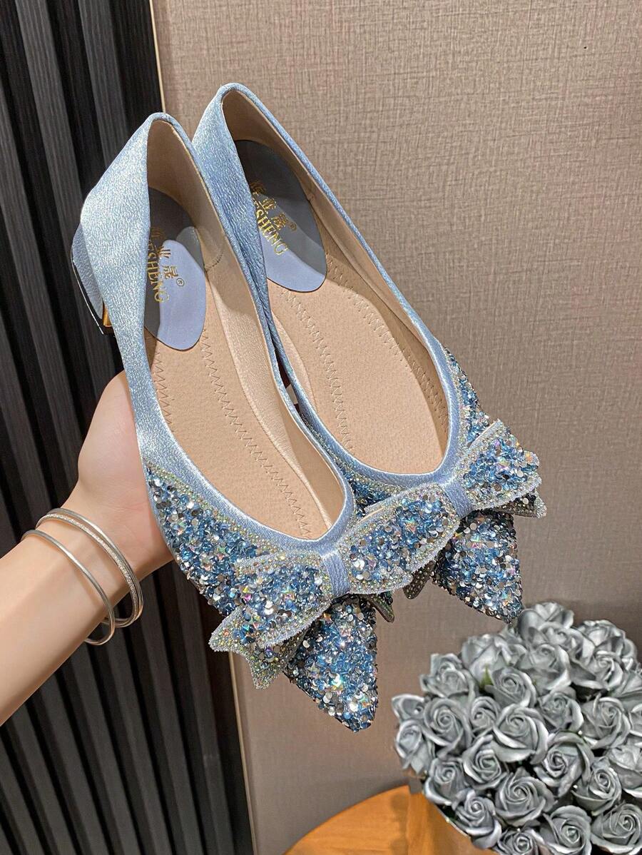 Held pair of icy blue rhinestone bow pumps with pointed toes and low block heels