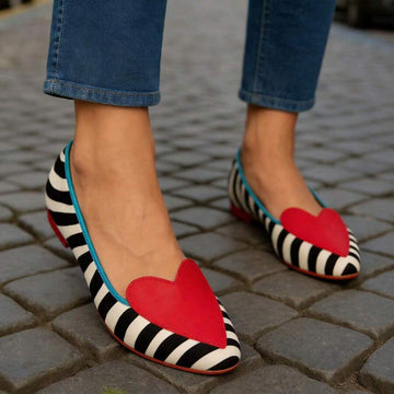 On-foot view of red-heart zebra stripe loafers with turquoise binding on cobblestones