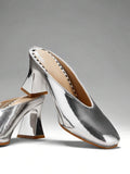Silver close three-quarter view of patent mule pumps with closed vamp, open back, softly squared toe, and flared block heel