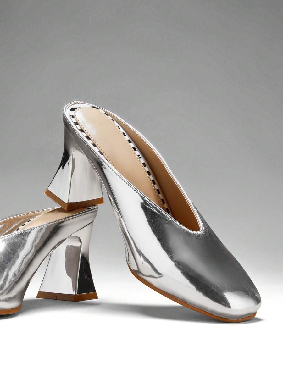 Silver close three-quarter view of patent mule pumps with closed vamp, open back, softly squared toe, and flared block heel