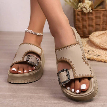 Khaki platform slide sandals on feet with rhinestone buckle and ribbed sole