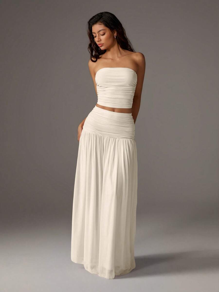 Elevate your style with this chic two-piece set featuring a cropped mesh bustier paired with a flowing maxi skirt. The solid color design offers versatile elegance, while the sheer mesh bustier adds modern sophistication. 
