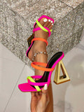 Neon pink lime and orange strappy mule sandal with gold triangular heel held close-up over rhinestone backdrop
