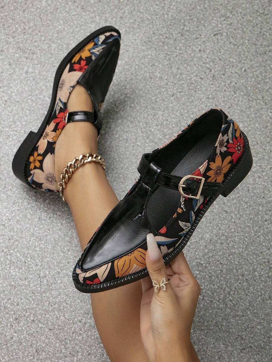 Held and worn black floral T-strap Mary Jane pumps with pointed toes and gold buckles