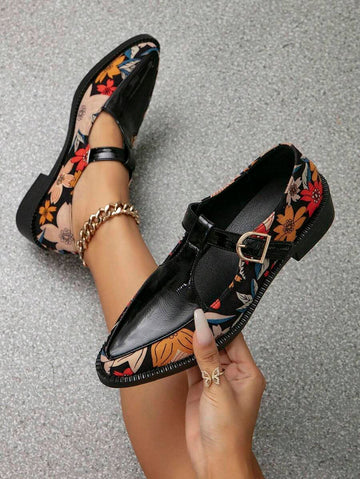 Held and worn black floral T-strap Mary Jane pumps with pointed toes and gold buckles