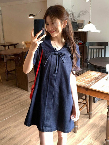 Three-quarter front view of dark-indigo sailor-collar denim mini dress with chest bow and short sleeves