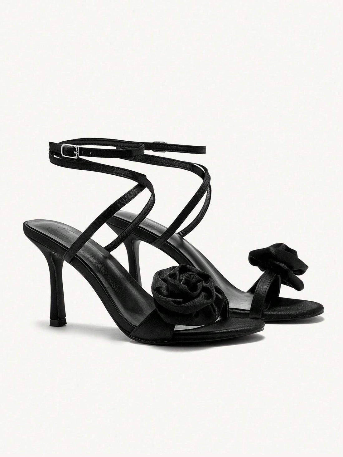 Black high-heeled sandals with floral details worn with a black ruffled skirt on a white background