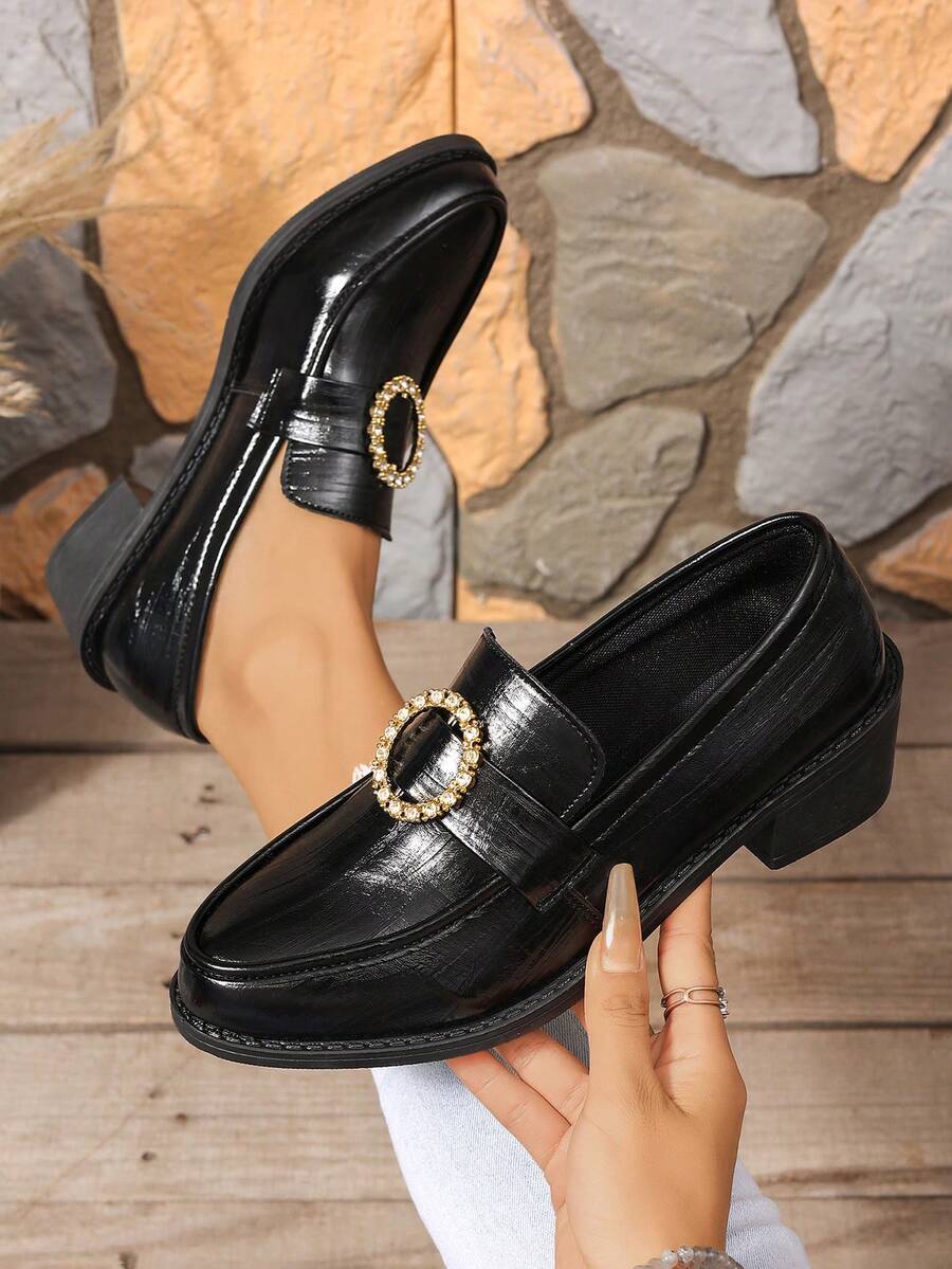 Close-up of black almond-toe loafer with gold-tone oval rhinestone buckle and low block heel